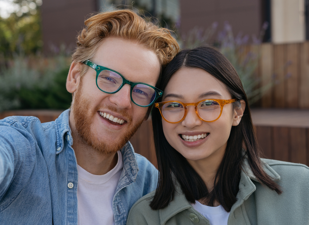 Smiling Couple Wearing Stylish Eyeglasses – Eyeglasses A cheerful young couple wearing modern prescription eyeglasses smiles together outdoors. Their frames feature bold colors and contemporary designs, highlighting both fashion and visual clarity – Eyeglasses.