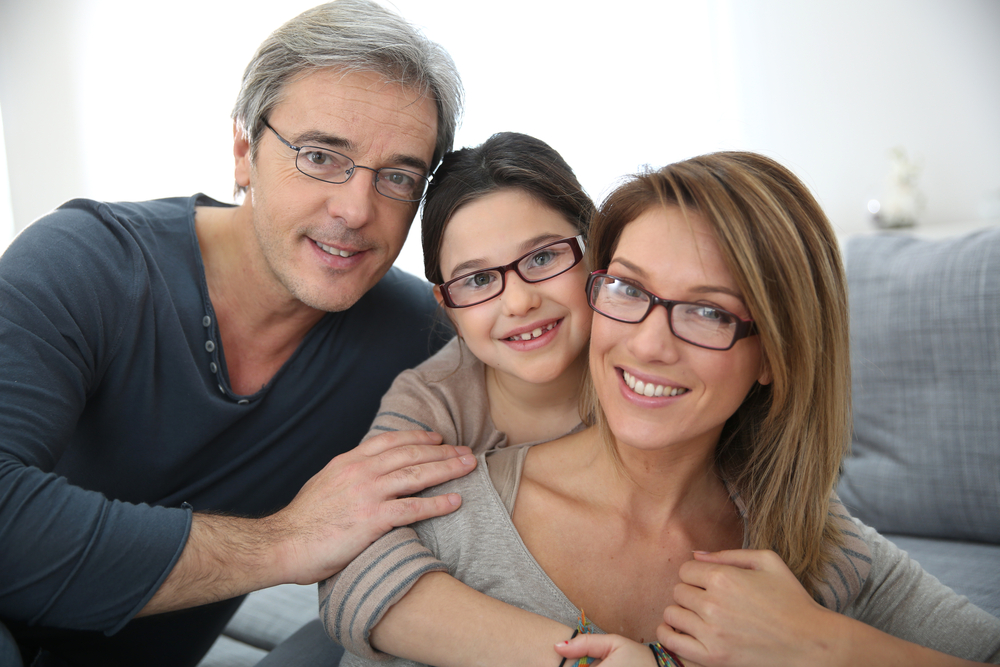 Happy Family Wearing Matching Eyeglasses – Eyeglasses A smiling family of three, all wearing stylish eyeglasses, poses together in their living room. Their coordinated frames emphasize comfort, clarity, and family-friendly eyewear options – Eyeglasses.