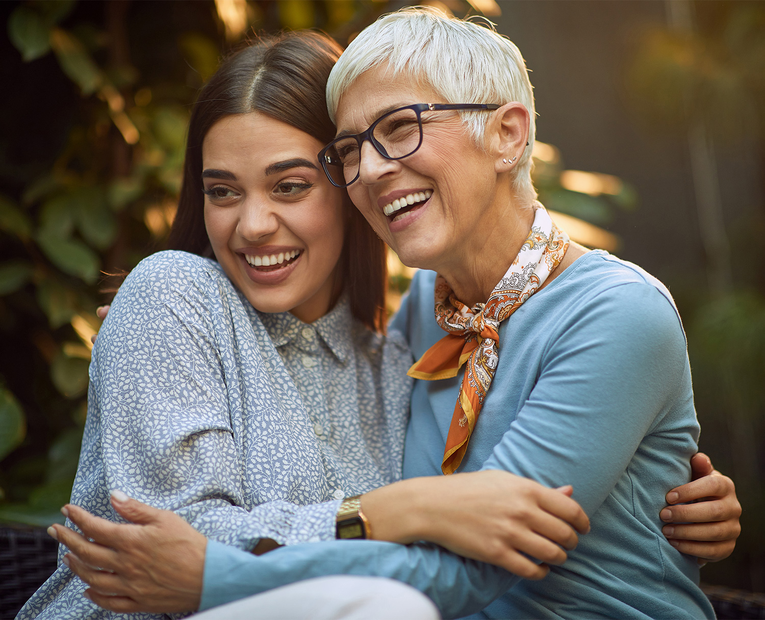 Two women, one older and one younger, share a warm hug while smiling and laughing together outdoors - Eye Doctor Rolla MO | Invision Family Eye Care